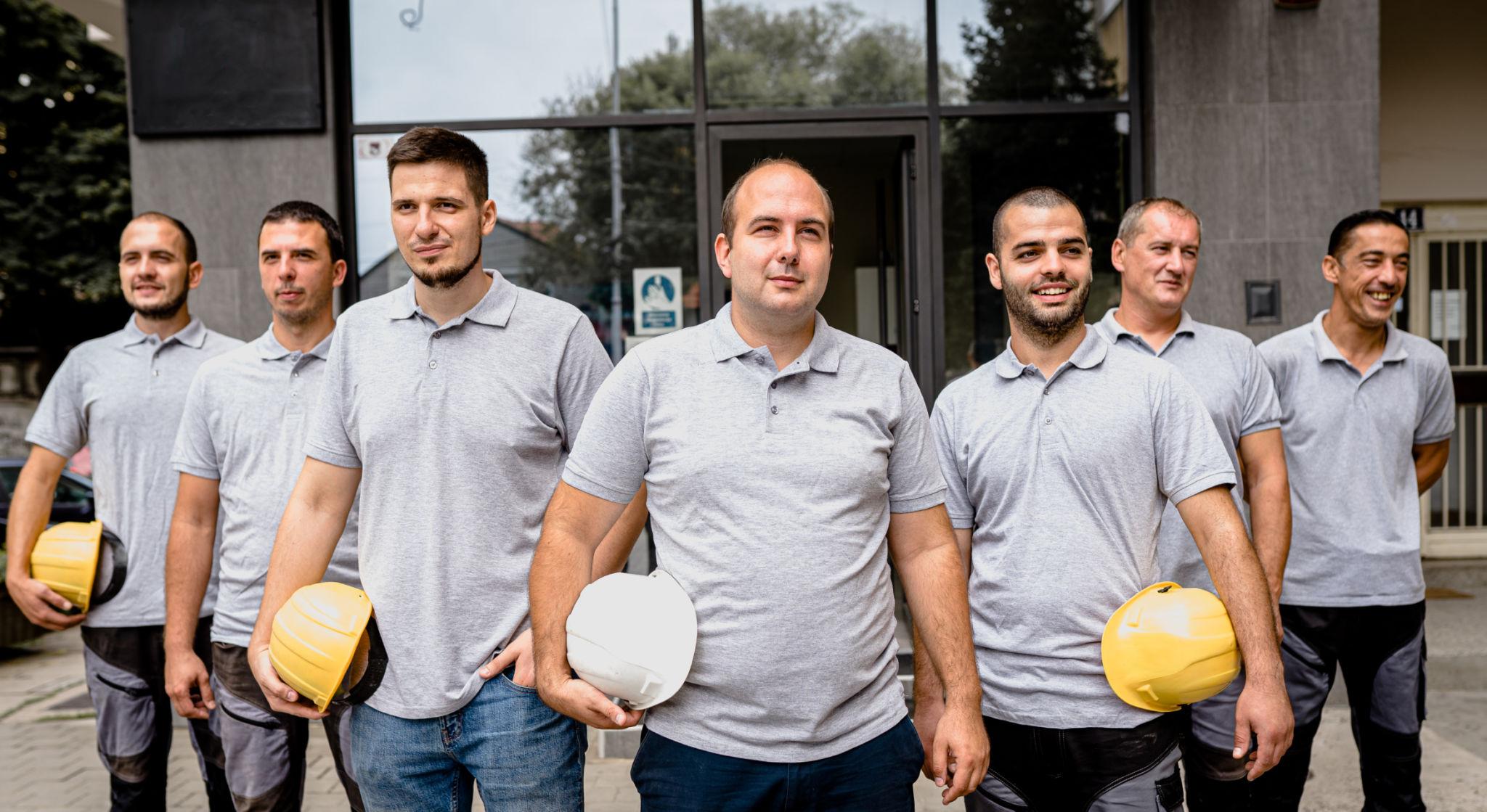Construction workers wearing branded T-shirts and hard hats standing together on a construction site, representing a professional and unified construction team identity.