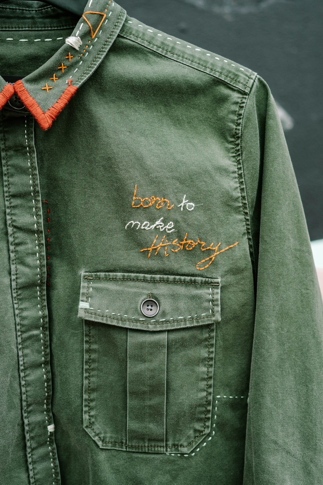 Close-up of an olive green embroidered workwear shirt with decorative stitching, chest pocket, and custom embroidery design showcasing premium garment customization.
