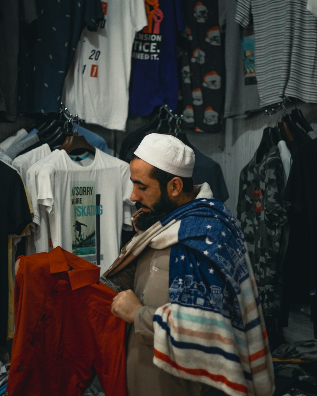 Customer shopping for clothing in a T-shirt store, examining a red shirt surrounded by graphic tees and casual apparel on display.